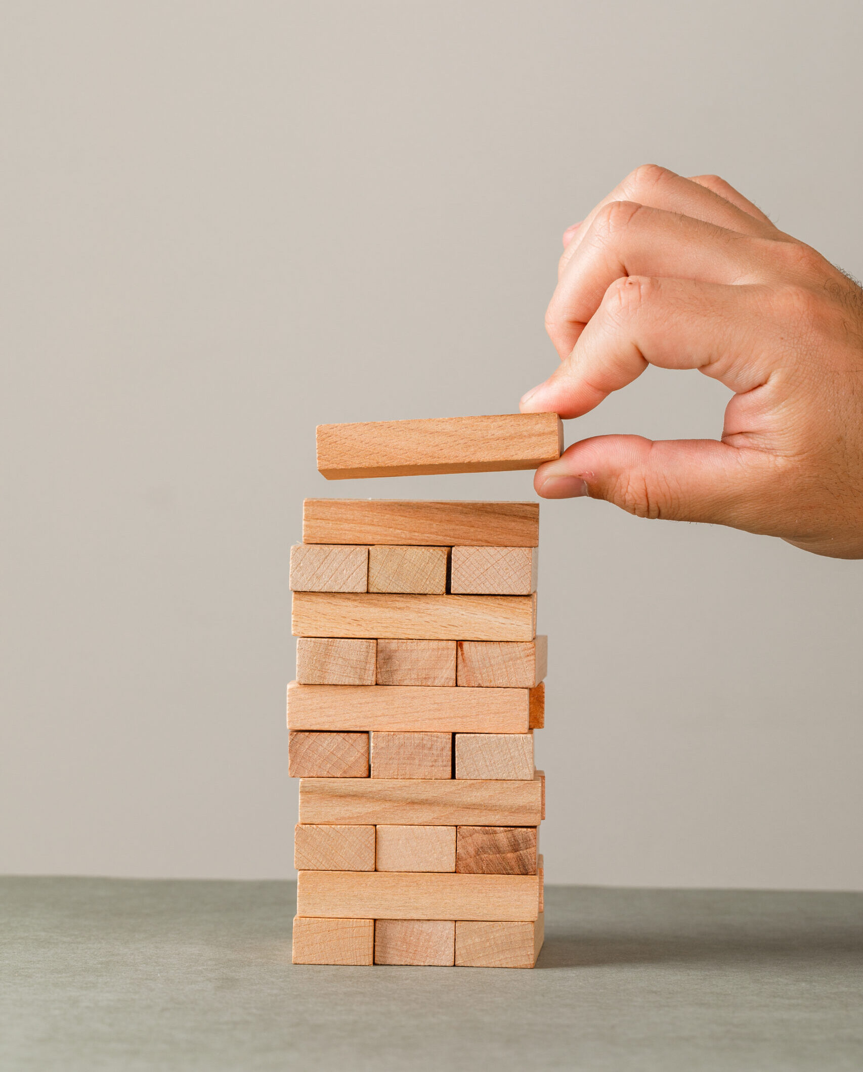 Business growth concept on grey and white background side view. hand putting wood block onto tower.